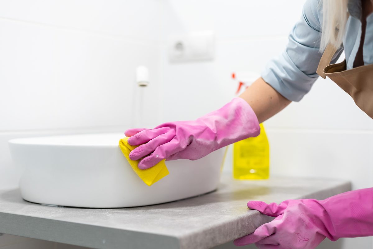 donna pulisce il lavandino con i guanti e una pezza